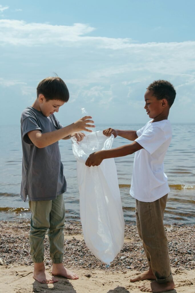 Two children picking up plastic trash on a sandy beach.