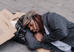 A homeless man sleeping on the street with cardboard signs and belongings.